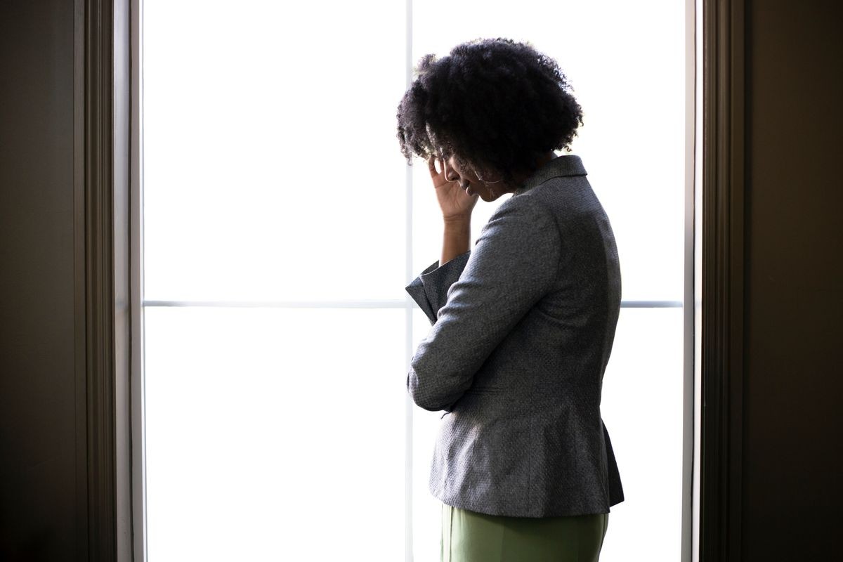 Silhouette of a stressed out black African American businesswoman looking worried and thinking about problems and failure by the office window.  She looks depressed or upset about debt or bankruptcy.